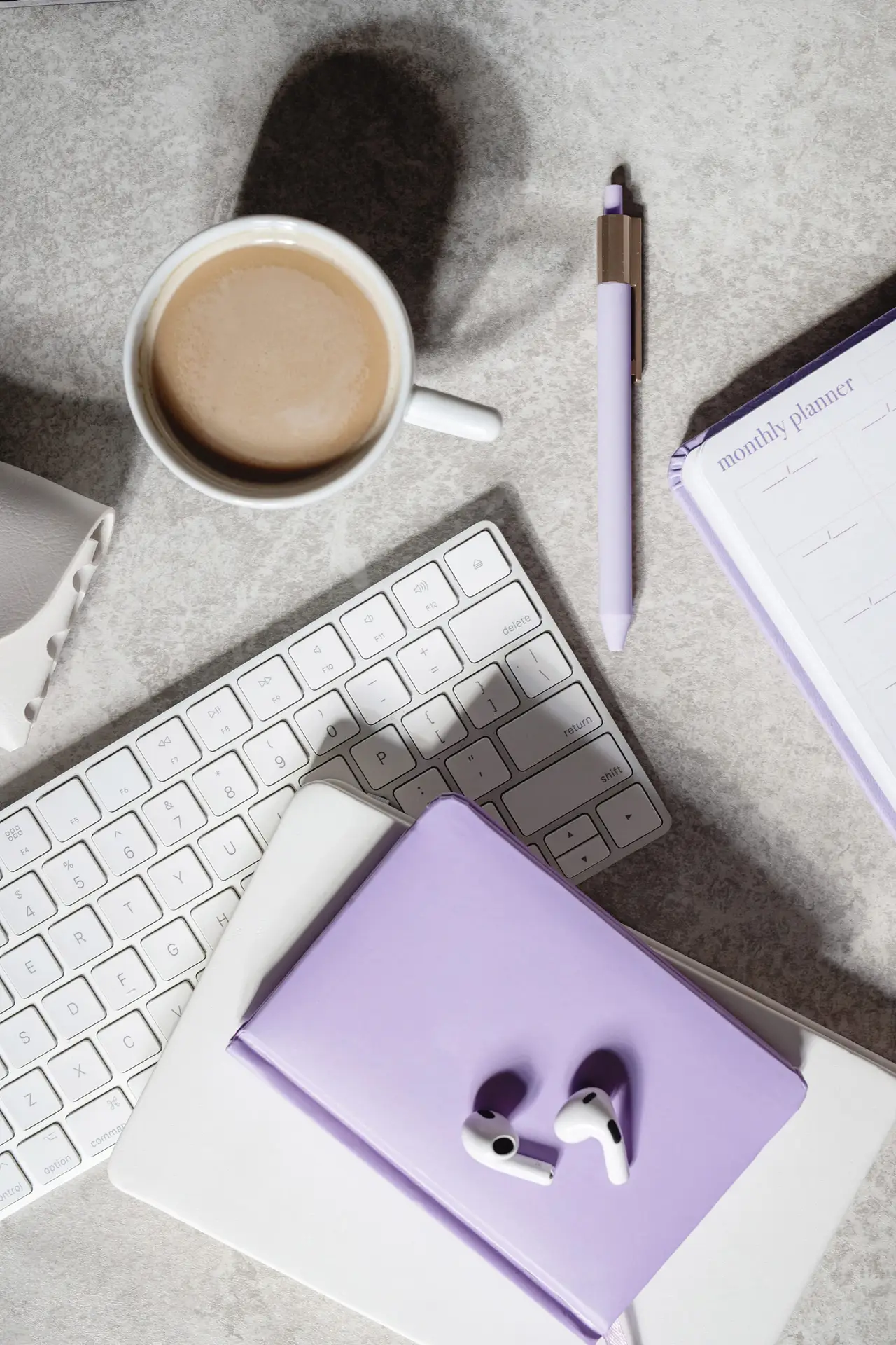 Desk with coffee cup, keyboard, pen, notebooks and ear buds